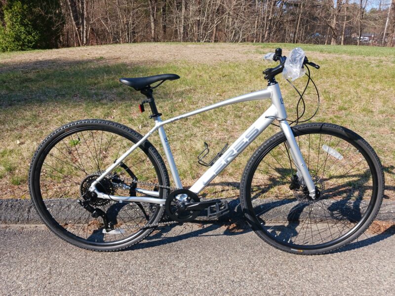 Picture of a white hybrid bicycle on the sidewalk next to a great park